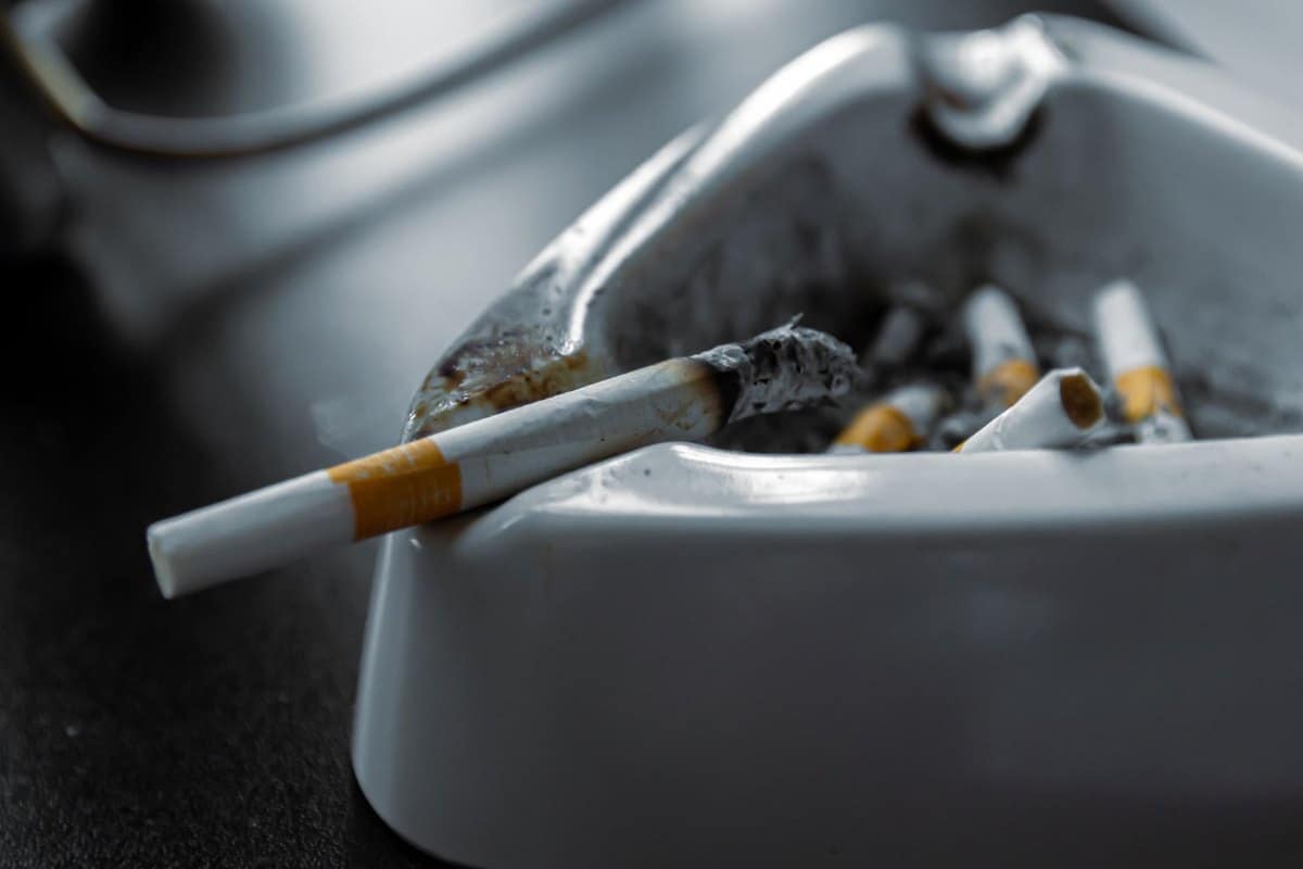 Cigarette posée sur un cendrier rempli de mégots