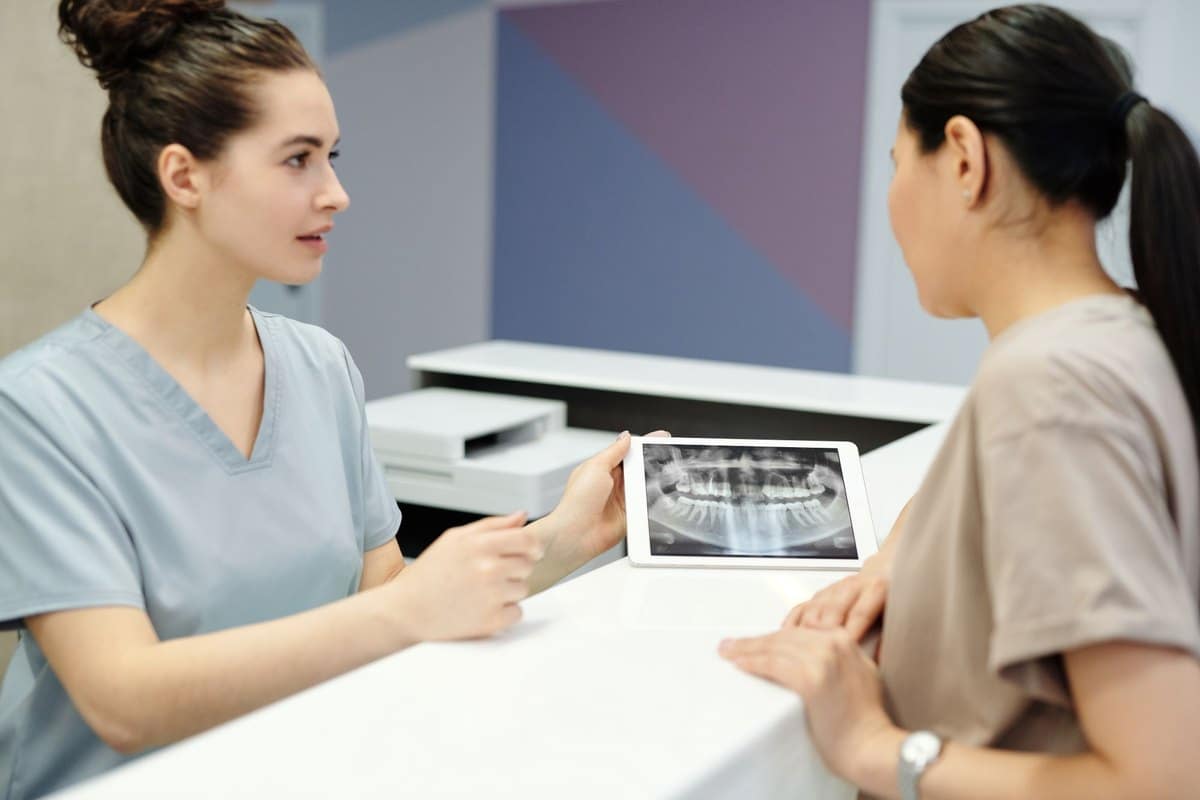 Praticienne montrant une radiographie dentaire sur tablette à une patiente